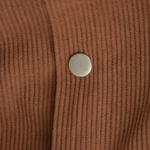 Macro detail of brown corduroy texture and matte metal snap button on high-waist skirt