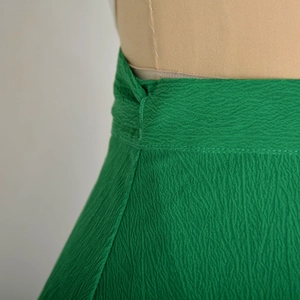 Close-up of emerald green skirt fabric with high-density pleated texture and stitching