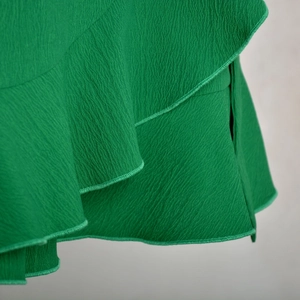 Detailed close-up of vibrant green ruffle fabric texture on a high-waisted wrap skirt