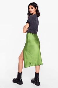 Detail view of the side slit and glossy satin fabric of the green midi skirt on model