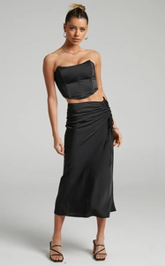 Detail of black satin two-piece set featuring structured corset top and ruched midi skirt