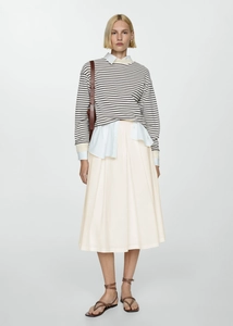 Detail showing creamy pleated midi skirt styled with layered knitwear and leather bag