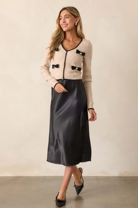 Détail d'une jupe en satin à taille haute avec un cardigan beige orné de nœuds