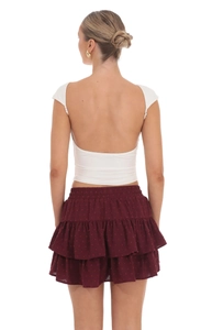 Detail of cross-back white crop top and burgundy tiered ruffle skirt with dot texture