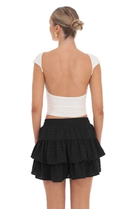 Detail of a white open-back crop top and black layered skirt with subtle dot texture