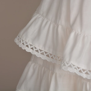 Detail of white tiered ruffle skirt with intricate geometric lace trim and fabric texture