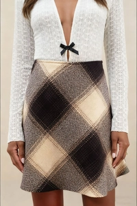 Close-up of white knit top with black bow and high-waisted plaid wool skirt details