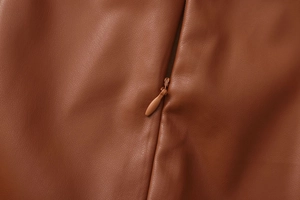 Close-up of high-quality brown PU leather texture and smooth invisible zipper detail
