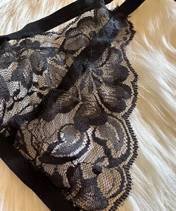 Detailed macro view of delicate black floral lace lingerie with eyelash trim on white plush