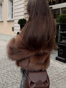 Detail of a brown faux fur jacket with thick texture and a stylish leather crossbody bag