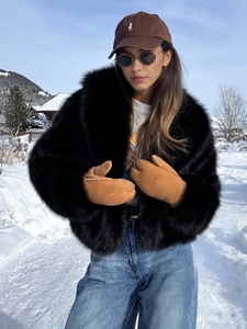 Detail shot of plush black faux fur coat and brown suede mittens in snow scenery