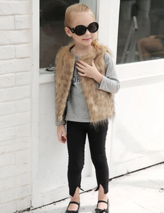 Fillette en gilet en fausse fourrure marron et t-shirt gris devant un mur de briques
