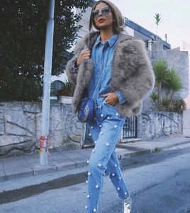 Dettaglio della giacca grigia in finta pelliccia e jeans decorati con perle bianche