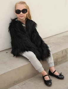Detail of girls' black faux fur coat showing plush texture and stylish outfit pairing