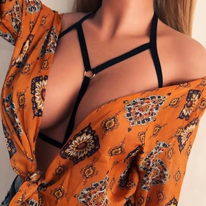 Close-up of black elastic cage bra with central silver metal ring on model wearing floral shirt