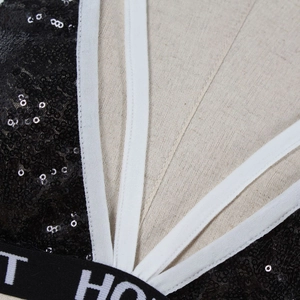 Detail of black sequined lingerie featuring white V-neck tape and lettered elastic band