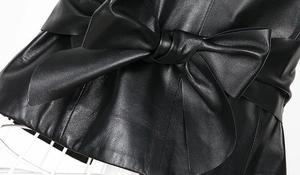 Detail shot of a black faux leather waist belt featuring a large decorative bow tie design