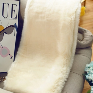 Detail of soft cream faux fur shawl draped on grey sofa with Vogue magazine