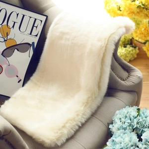 Luxurious faux fur shawl in cream white displayed on a grey sofa with elegant decor