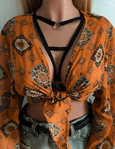 Détail d'un crop top bohème orange à fleurs avec des lanières noires et des manches longues
