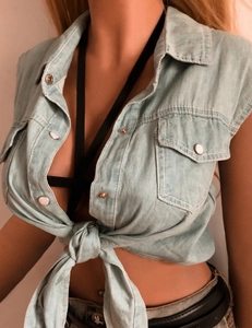 Dettaglio di un crop top in denim lavato azzurro con nodo frontale e bottoni metallici