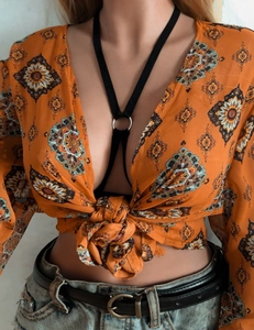 Dettaglio del top corto boho arancione con lacci e accessorio imbracatura con anello