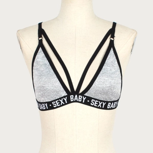 Detail of cross-strap sports bra with SEXY BABY elastic band on gray fabric