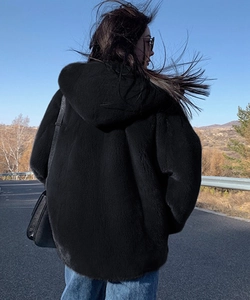 Back view of a black oversized faux fur hooded jacket styled with a crossbody bag on a road