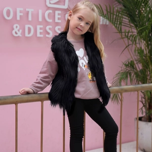 Mädchen in stylischer schwarzer Kunstpelzweste und rosa Sweatshirt vor rosa Wand