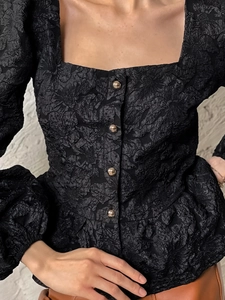 Close-up of black jacquard fabric texture and decorative gold buttons on square neck top