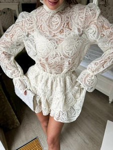 Dettaglio del tessuto in pizzo bianco con motivi paisley sul top a maniche lunghe