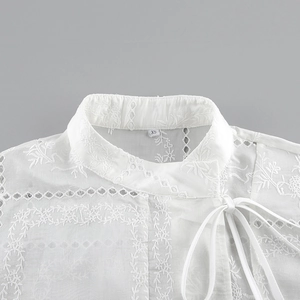 Detalle de los bordados de estilo chino y encaje calado en una blusa de algodón blanca