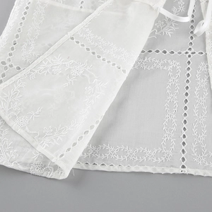 Detalle de tela bordada blanca con motivos florales calados y una cinta ajustable