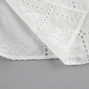 Detalle de blusa de algodón blanca con bordados florales y diseño de encaje calado