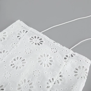 Dettaglio di ricamo inglese in cotone bianco con motivi floreali e spalline sottili