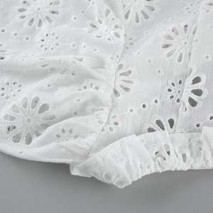 Dettaglio ravvicinato del top in cotone bianco con ricami floreali e inserti traforati