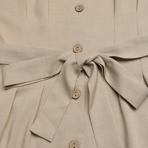 Detail of wooden buttons and waist tie belt on a beige casual sleeveless jumpsuit
