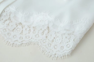 Close-up of delicate white eyelash lace trim with floral patterns on a long sleeve top