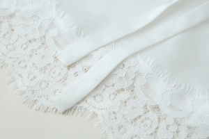 Detailed close-up of white eyelash lace trim and smooth satin ribbon ties on a blouse