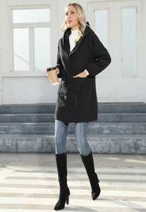 Profile view of a long black hooded windbreaker paired with denim jeans and tall black boots