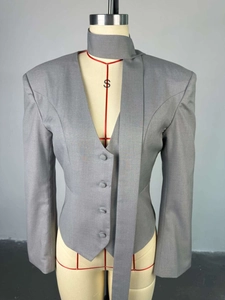 Détail d'un blazer gris cintré avec col en V, fermeture boutonnée et détail écharpe assorti