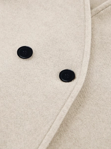 Close-up van beige wollen jas met dubbele rij zwarte knopen en verfijnde textuur