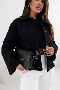 Détail d'une veste en laine noire avec poches à rabat et sac en cuir à boucle dorée