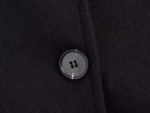 Detailed close-up of a black wool jacket featuring a marbled four-hole button accent