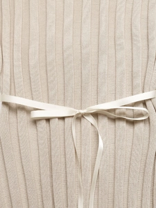 Détail d'une robe en maille beige avec texture côtelée et nœud en satin blanc à la taille