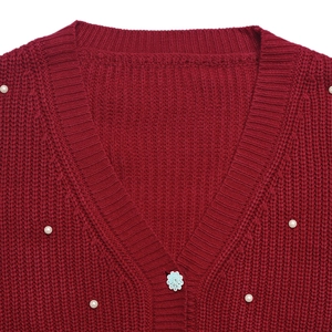 Close-up of red knit cardigan featuring elegant white pearls and a flower buckle detail