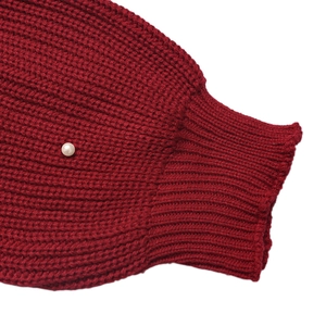 Close-up of chunky red knit sleeve with ribbed cuff and elegant white pearl detail