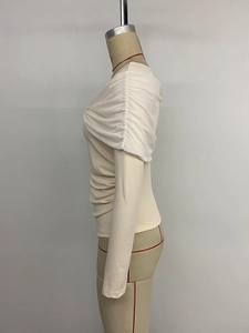 Detailed view of the layered pleats and sheer tulle fabric on the off-shoulder beige top