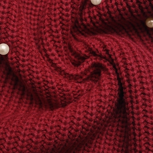 Close-up of red chunky knit sweater fabric featuring delicate white pearl embellishments