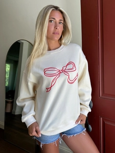 Detail of red bow tie embroidery on a cream casual long-sleeve crewneck sweatshirt